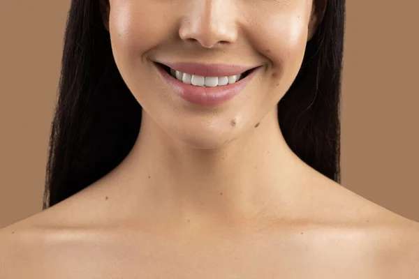 Anti-aging treatment. Cropped shot of smiling lady posing topless isolated on beige studio background, unrecognizable woman showing her beautiful young smooth skin, perfect white teeth