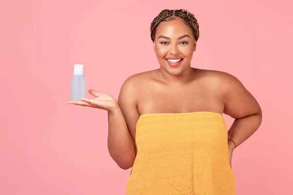 ボディ正アフリカ系アメリカ人女性保持マイクロセラーウォーターボトル 広告新しい化粧品 ピンクの背景の上にポーズ スタジオショット — ストック写真