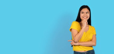 Sarı tişörtlü Japon bayan öğrencinin boş alana bakıp mavi arka planda, stüdyoda, panoramada izole edilmiş yeni bir düzen düşünmesine sevindim. Harika reklam ve teklif, satış, insani duygular.