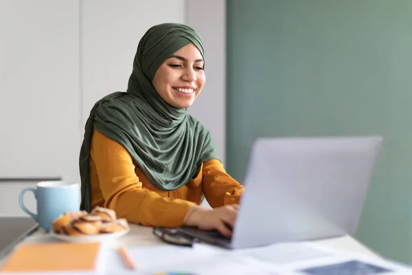 オンライン教育の概念 自宅でノートパソコンを使ってヒジャブ州の若いムスリム女性を笑顔にし 机の上に座ってキーボードを押したり 距離学習を楽しんだり — ストック写真