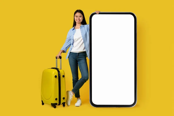 穿着休闲装 头戴手提箱 带着巨大智能手机 背景为黄色 工作室的空白屏风的千年韩国女学生游客的微笑 旅行设备 地图应用程序 广告和报价 — 图库照片