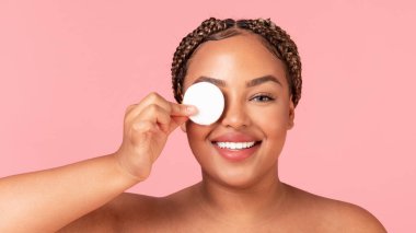 Siyah vücutlu, mükemmel ciltli, pamuklu ped ile makyaj yapan, pembe arka planda poz veren, panorama yapan bir kadın. Yüz temizleme, güzellik, tedavi ve doğal kozmetik konsepti