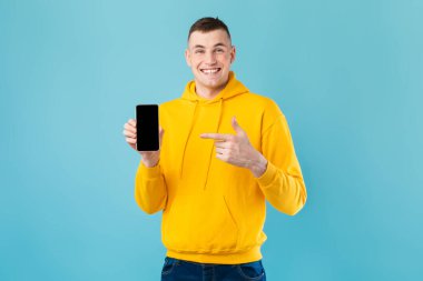 Heyecanlı beyaz adam siyah ekranlı akıllı telefon gösterisi yapıyor ve onu işaret ediyor. Mavi stüdyo arka planında boş yer var.