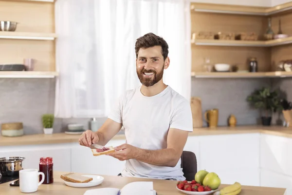 快乐的中年白人男性 留着胡子 穿着白色T恤 早餐做三明治 周末愉快 在现代厨房的内部自由自在 一个人早上好 家里有健康的食物 — 图库照片