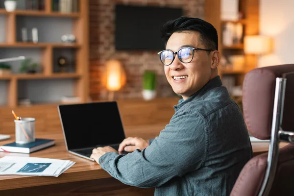 戴着眼镜微笑的亚洲中年商人在电脑上工作 屏幕空白 坐在办公室的桌子前 现代商业 远程自由职业 投资和技术网站 — 图库照片