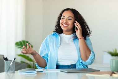 Mutlu Afro-Amerikan kadın portresi. Akıllı telefondan konuşan, evde masa başında oturan, boş alan. Heyecanlı siyah kadın telefon görüşmesi yapıyor.
