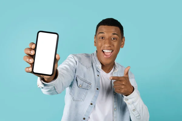 酷网站 心满意足的年轻非洲裔美国人指着智能手机用蓝色背景的空屏幕工作室 咨询和推荐 应用程序演示 广告和报价 — 图库照片
