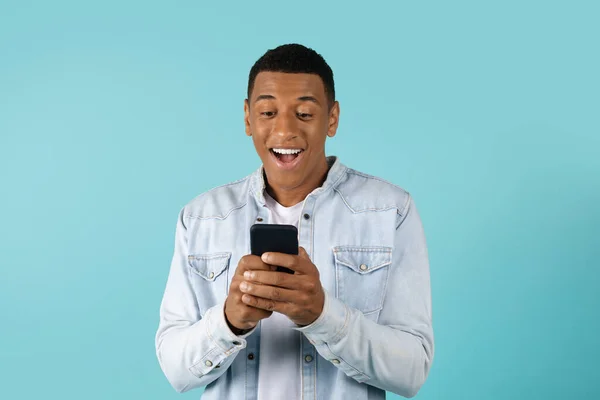 惊讶的笑着年轻的非洲裔美国人在智能手机上随意打字孤立的蓝色背景 伟大的广告和提供 聊天和社交网络应用 好消息 通信技术 — 图库照片