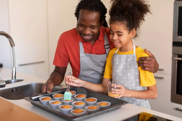 幸せな黒の父と娘キッチンで一緒にマフィンを焼く 卵の黄身とペストリーのトップをブラッシングアフリカ系アメリカ人の少女 自宅で彼女のお父さんと一緒に料理を楽しむ フリースペース — ストック写真