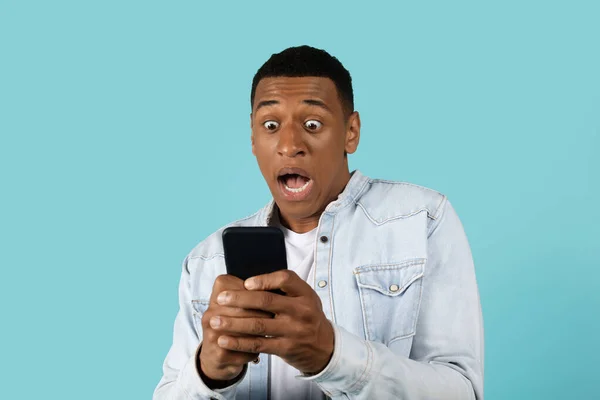 恐惧震惊可笑的年轻的非洲裔美国人在休闲与张开的嘴尖叫 手机孤立的蓝色背景 害怕面部表情 人类情感 应用程序和对坏消息的反应 — 图库照片