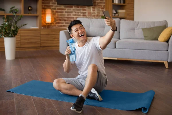 兴奋的韩国成熟男人一边休息 一边用手机自拍 坐在瑜伽垫上 快乐的亚洲男子在网上与私人教练交谈 — 图库照片