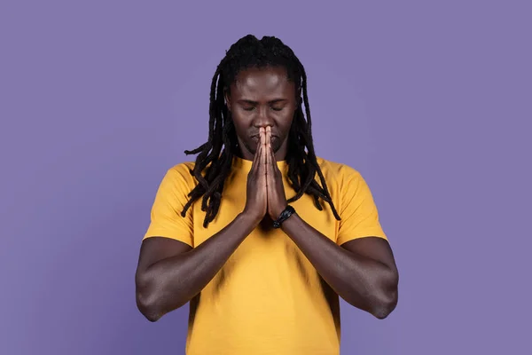 穏やかな精神的なハンサムなアフリカ系アメリカ人の若者は目を閉じて祈る 手の瞑想に参加して真剣な平和的な男 紫色のスタジオの背景に隔離されました 信念の概念 コピースペース — ストック写真