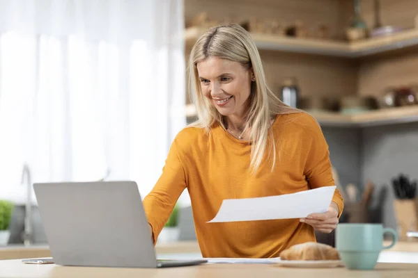 쾌활하게 매력적 프리랜서 가집에서 일하면서 노트북을 식탁에 서류를 미소를 부인은 — 스톡 사진