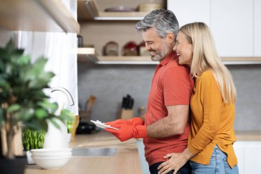 Yakışıklı, orta yaşlı, kır saçlı koca mutlu karısına ev işlerinde yardım ediyor, yemekten sonra bulaşıkları yıkıyor, sohbet ediyor, gülümsüyor, sarılıyor, yan gözle bakıyor, mekanı kopyalıyor.