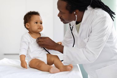Çocuk Sağlığı Hizmetleri. Pediyatrist Doktor, siyah bebek hastasıyla kontrol sırasında stetoskop kullanıyor. Afrikalı Amerikalı pediatrist, klinikteki çocukla tıbbi kontrol yapıyor.