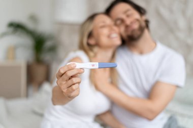 Mutlu beyaz eşler pozitif hamilelik testi gösteriyor ve evde kucaklaşıyorlar, seçici odaklanma. Sevgili koca ve eş müstakbel anne baba olacağımız için heyecanlı hissediyoruz. Aile planlaması konsepti