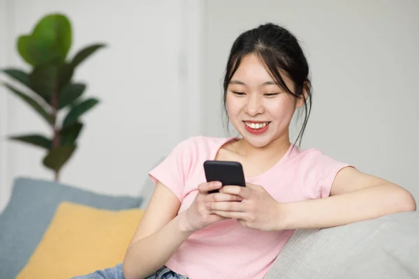 興奮した韓国の女性はソファに座って スマートフォンを使用して 友人とオンラインでチャットし 無料のコピースペース 携帯電話がソファで凍ってる可愛い女性ソーシャルメディアをチェック — ストック写真
