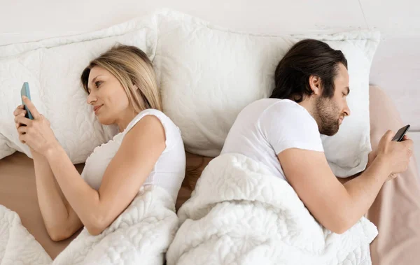 婚姻危机 白种人夫妇使用手机 背靠背躺在床上 对彼此漠不关心 高瞻远瞩 夫妻之间相互不理睬 在家里给情人发短信 — 图库照片