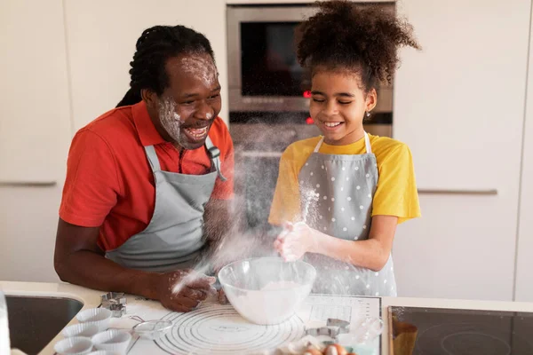 Joyful Black Father And Daughter Having Fun While Baking In Kitchen, Happy African American Dad And Preteen Female Child Fooling Together While Cooking Pastry, Girl Playing With Flour And Making Clap