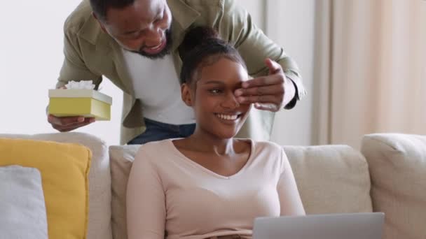 一起生活的快乐年轻漂亮的非洲裔美国女人在家里用笔记本电脑玩耍 她心爱的男朋友来了 并做出了令人惊讶的礼物 跟踪镜头 慢动作 自由自在的空间 — 图库视频影像