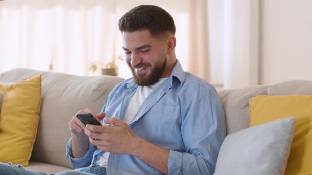 年轻的中东人喜欢用智能手机上网 喜欢家里的社交媒体新闻 躺在沙发上 跟踪镜头 慢动作 — 图库视频影像