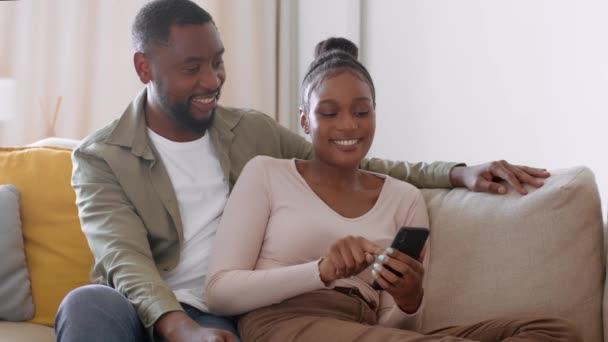 若い幸せなアフリカ系アメリカ人の夫婦は家で一緒に休んで スマートフォンでサーフィンし 週末の活動を計画し 撮影を追跡し スローモーション 空のスペース — ストック動画
