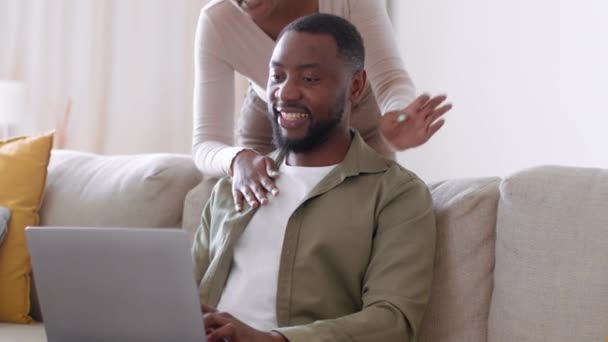 远程工作的好处 年轻的黑人自由职业者在家里的笔记本电脑上打字 他心爱的女朋友走过来拥抱他 一起看笔记本电脑 跟踪镜头 慢动作 自由自在 — 图库视频影像