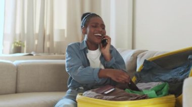 Genç ve güzel Afrikalı Amerikalı bayan telefonda konuşuyor, tatil planlarını tartışıyor, bavul ve biletleri kontrol ediyor, seyahat beklentisi, izleme çekimi, yavaş çekim, serbest alan