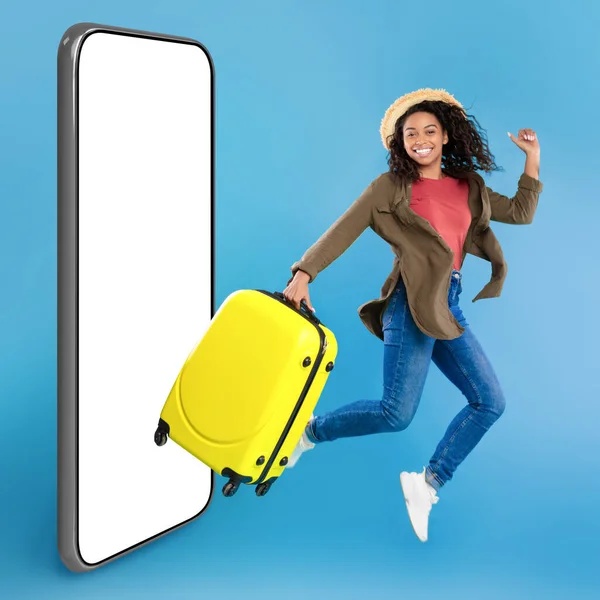 Приложение Путешествий Возбужденная Молодая Черная Женщина Ярким Чемоданом Прыгает Смартфону — стоковое фото