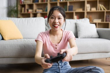 Kanepede oturup joystickle online oyun oynayan mutlu Çinli kadın, evde boş zamanın tadını çıkarıyor. Hafta sonu dinlenme, teknoloji ile hobiler ve eğlence