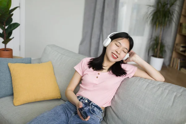 現代のワイヤレスヘッドフォンで音楽を聴いているかなりアジアの女性は 自宅で休んで 閉じた目で好きな曲を楽しんでいます 国内エンターテイメント クールな趣味の概念 — ストック写真
