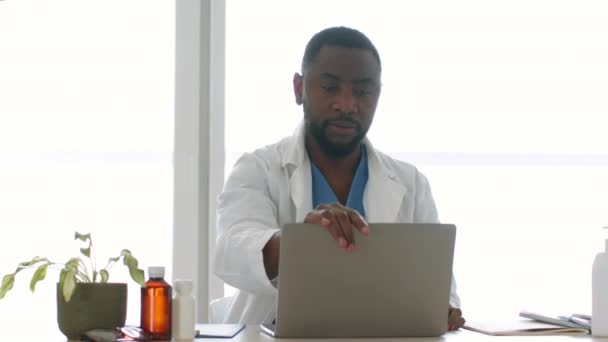 专业医学概念 年轻的非洲裔美国医生打开笔记本电脑 开始打字 检查病人早上在办公室的时间安排 跟踪拍摄 慢动作 空旷的空间 — 图库视频影像