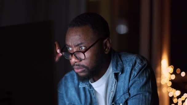 過労の概念 コンピュータ上で慎重に電子メールを読んで眼鏡をかけて若い濃縮されたアフリカ系アメリカ人男性の肖像画を閉じます 夜遅く家で働いて スローモーション フリースペース — ストック動画