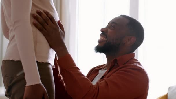 誠実な父の愛 幸せな若いアフリカ系アメリカ人男性抱擁し 彼の妊娠中の妻の大きな腹を撫でて 赤ちゃんのバンプを感じ 自宅で笑って 撮影を追跡し スローモーション フリースペース — ストック動画