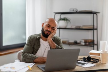 Ev ofisindeki dizüstü bilgisayarın önünde oturan ve ekranda boş alana bakan aşırı çalışan, üzgün Latin adam. Çalışan erkek ya da serbest çalışan iş yerinde bitkin düşmüş.