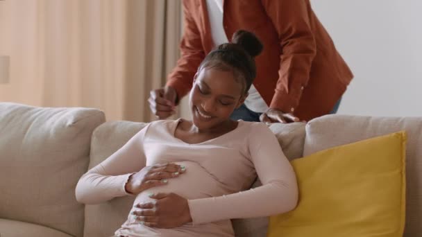 怀孕的快乐 年轻快乐的怀孕黑人妇女躺在沙发上 她心爱的丈夫过来爱抚大肚子 一起呆在家里 跟踪镜头 慢动作 空荡荡的空间 — 图库视频影像