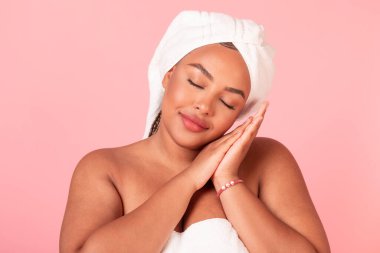 Güzellik uykusu kavramı. Siyah kadın uyukluyor, pembe stüdyo arka planında uyuyormuş gibi yapıyor. Afrikalı Amerikalı iri yarı kadın elleri kapalı, gözleri kapalı dinleniyor.