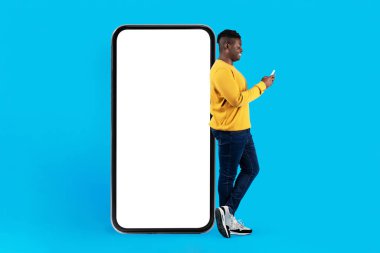 Mobil Model. Beyaz Ekranlı Büyük Boş Telefonun yanında duran Genç Boş Adam Mavi Arkaplan, Gülümseyen Afrikalı Amerikalı Adam Yeni Uygulama ya da Web Sitesi, Kolaj
