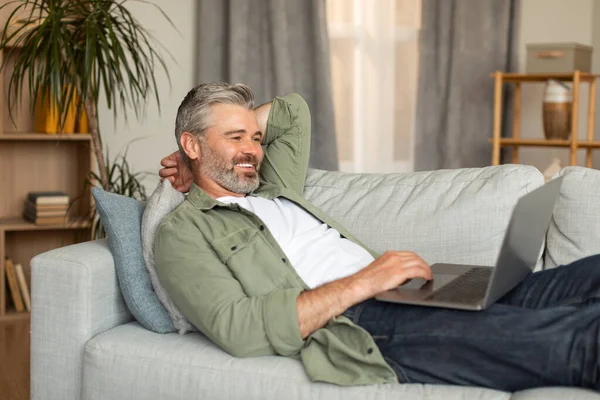Gülümseyen Beyaz Bir Adam Bilgisayarda Yazı Yazıyor Dinleniyor Kanepeye Uzanıyor — Stok fotoğraf