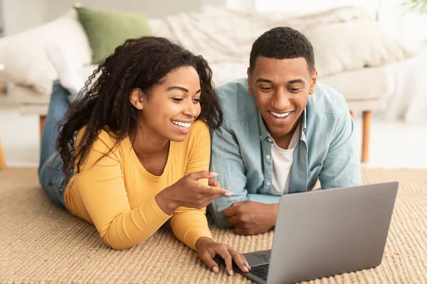 幸せな若いアフリカ系アメリカ人の女性と男性が床に横たわって ラップトップでチャットし 面白いビデオを見て リビングルームのインテリアでインターネットでサーフィンします 現代の技術 オンラインゲーム 一緒に自宅でビデオ通話 — ストック写真