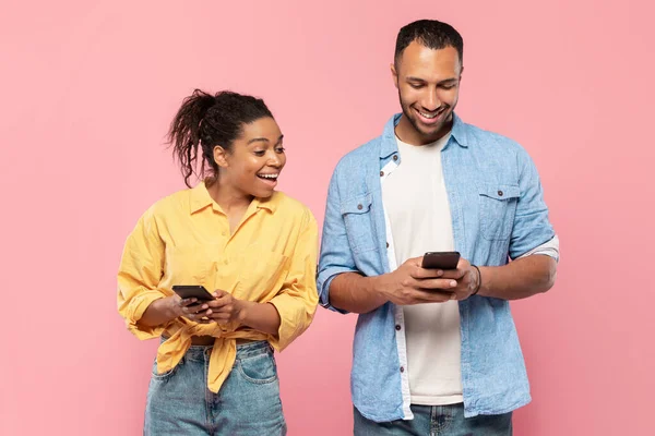 好奇心旺盛な黒人女性は彼女のボーイフレンドの携帯電話を見て 男は彼のガジェットを使用して チャット ピンクのスタジオの背景に一緒に立って — ストック写真