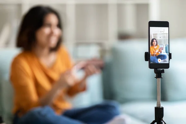 年轻的阿拉伯美容师在家里记录化妆评论 为她的博客拍摄视频内容 在相机上演示眼影调色板 在三脚架上使用智能手机 有选择地聚焦于设备 — 图库照片