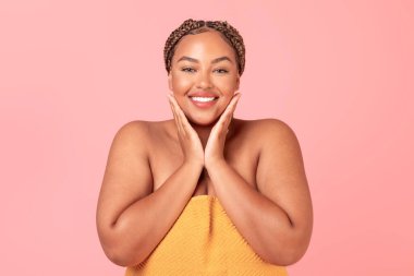 Cilt bakımı. Mutlu Afro-Amerikan kadın yüzüne dokunuyor ve gülümsüyor, güzel siyah kadın pembe arka planda poz veriyor, stüdyo çekimi.