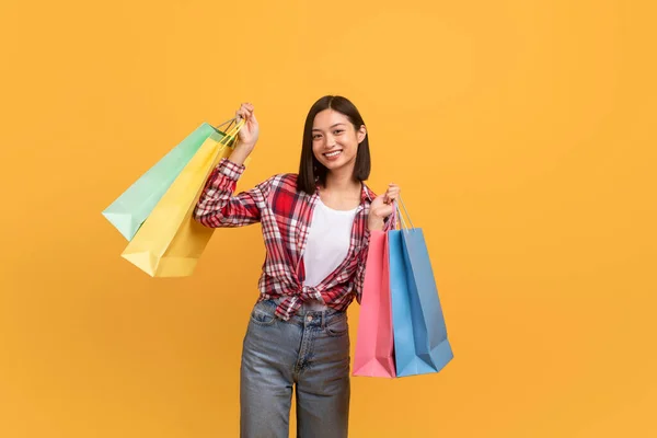 季节性销售概念 兴奋的亚洲女性顾客站在购物袋旁 为她在黄色工作室背景下的新购买而感到高兴 — 图库照片