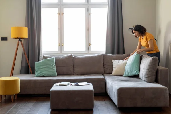 Mujer Árabe Joven Esponjando Cojines Sofá Mientras Limpia Casa Sonriendo —  Fotos de Stock