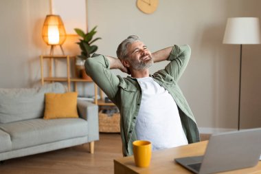 Tatmin olmuş, gevşemiş, yaşlı, beyaz bir erkek bilgisayarla masaya oturuyor, oturma odasında dinleniyor, rahatlığın, sessizliğin ve boş zamanın tadını çıkarıyor. Hafta sonu evde yalnızım, işten ayrılıyorum, rahatlıyorum, keyfim yerinde.