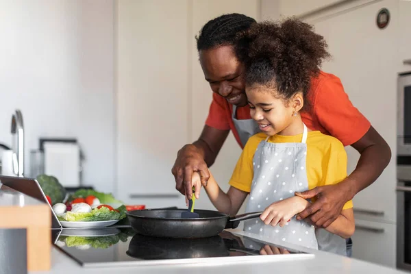 調理時間 家庭でアフリカ系アメリカ人の父親が女性の子供と一緒に健康的な食べ物を作るのを世話し一緒においしい食事を作る — ストック写真