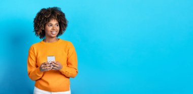 En yeni mobil uygulama. Portakallı gür saçlı, mutlu ve şık bir bayan cep telefonu kullanıyor ve mavi stüdyo arka planındaki reklam için fotokopi odasına bakıyor.