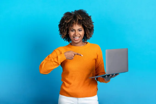 不错的在线报价 应用程序 有魅力的年轻黑人女士 满头浓密的秀发在线购物 手持现代笔记本电脑 指着电脑屏幕 微笑着 摆出一副蓝色画室的样子 复制空间 — 图库照片