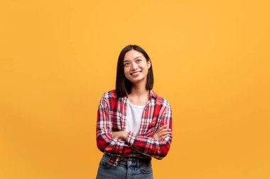 Rüya gören pozitif Asyalı kadın kollarını kavuşturmuş ve yana bakıyor, sarı arka planda poz veriyor, boşluğu kopyalıyor. Kadın güzel bir teklif düşünüyor.